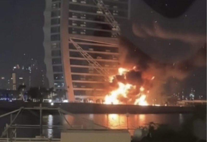 Burj Al Arab at night with a subtle hint of smoke or flames, symbolizing the drone scare and its market repercussions.