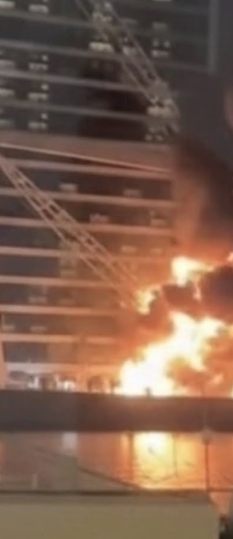 Burj Al Arab at night with a subtle hint of smoke or flames, symbolizing the drone scare and its market repercussions.