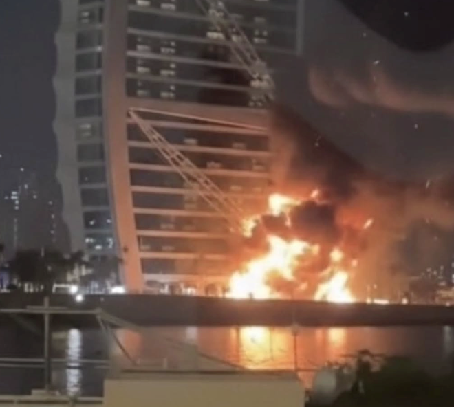 Burj Al Arab at night with a subtle hint of smoke or flames, symbolizing the drone scare and its market repercussions.